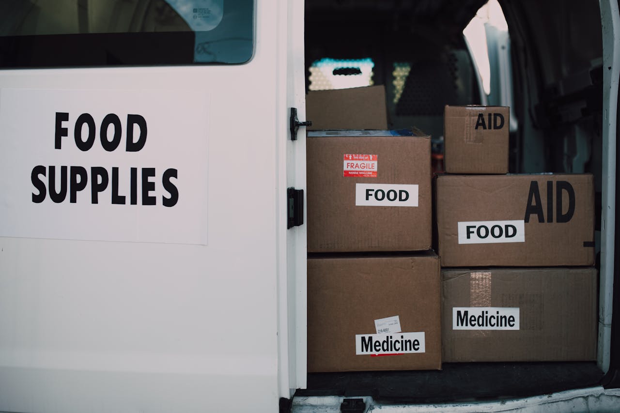 Stacked donation boxes labeled food and medicine in a delivery van for charity aid.