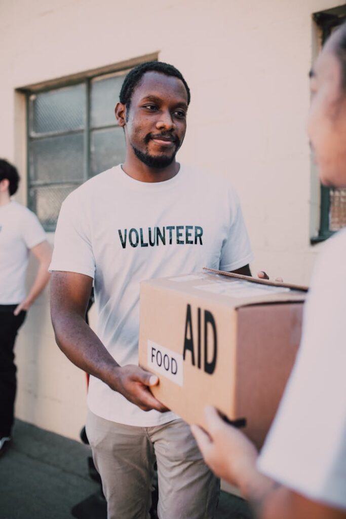 A volunteer hands a box labeled 'aid' and 'food' during an outdoor charity event.